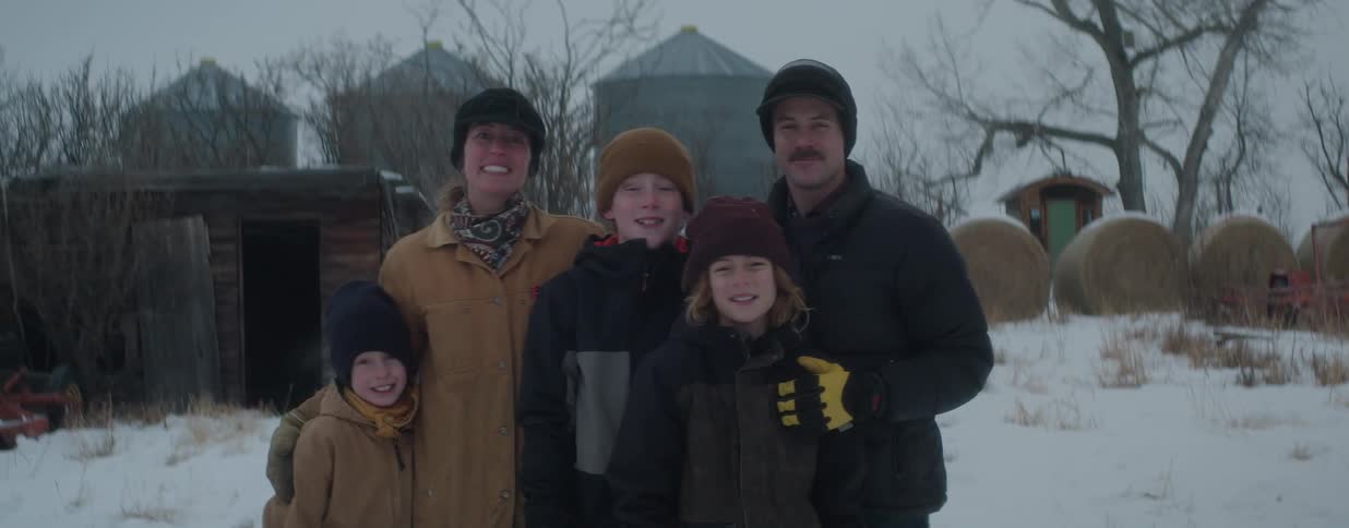 A happy family of five poses for a winter portrait on their snowy, rural farm
