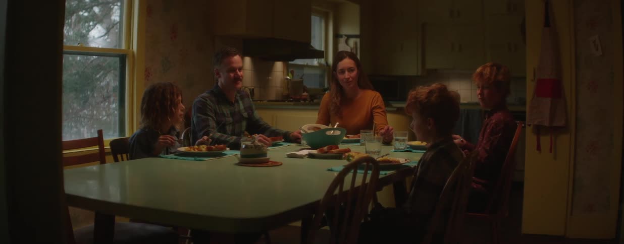 A happy family with three sons enjoys a lively dinner together, laughing and talking in their warm and cozy kitchen