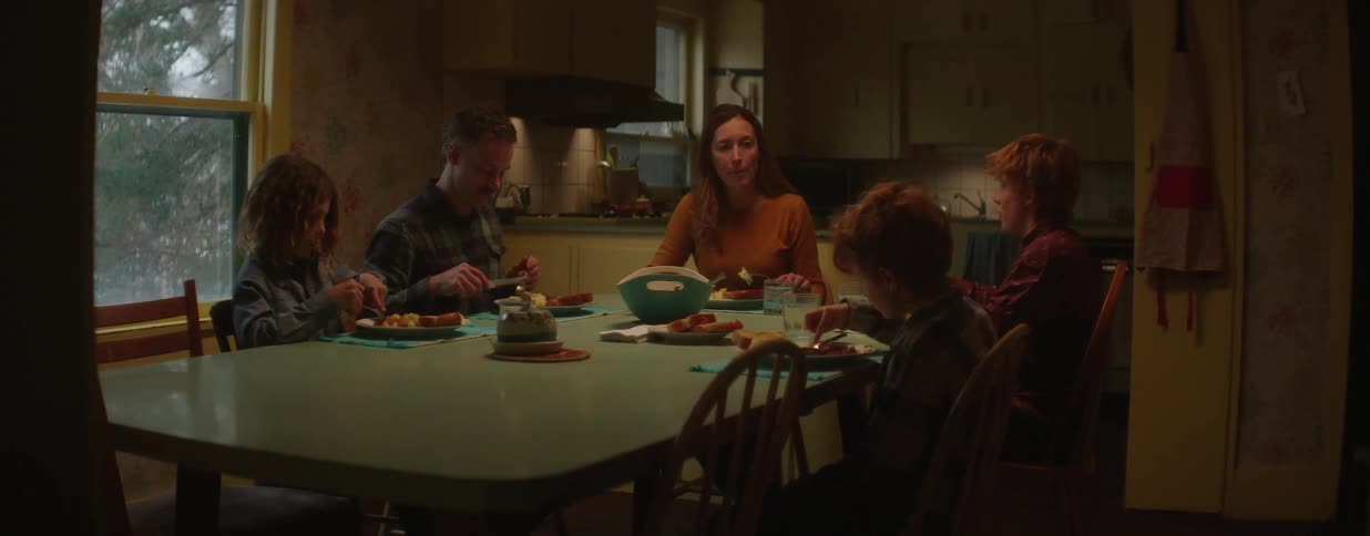 A family of five sits down together for a warm, intimate dinner in their cozy kitchen, sharing a meal and conversation
