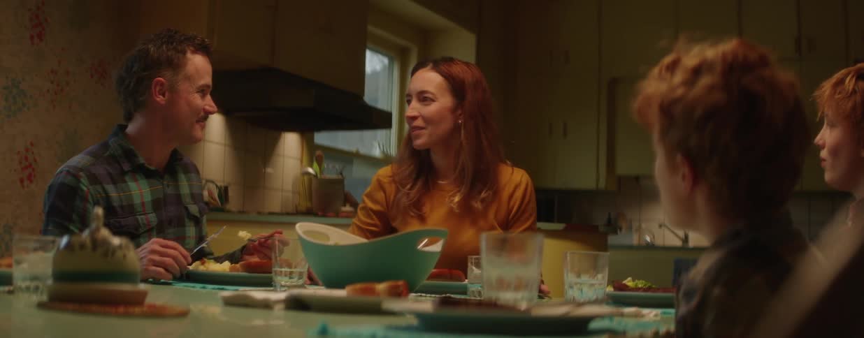 A mother laughs heartily as her family enjoys a warm and cozy dinner together in their kitchen