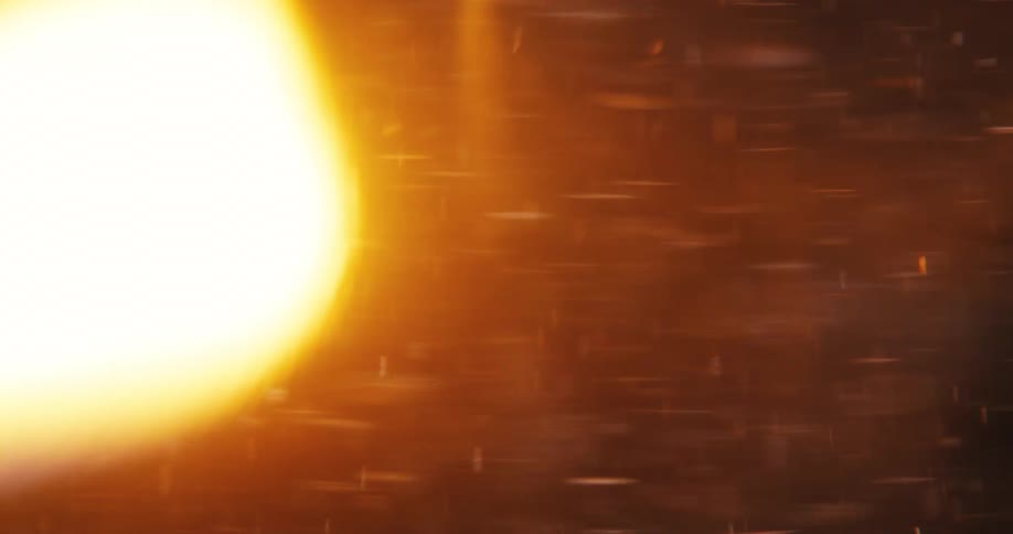 A dynamic abstract animation shows golden particles and a bright, warm lens flare swirling against a dark background