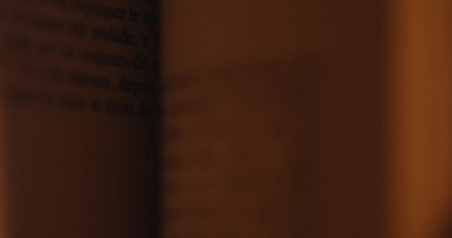 An out-of-focus close-up shot of pages turning in a book illuminated by a warm, dim light