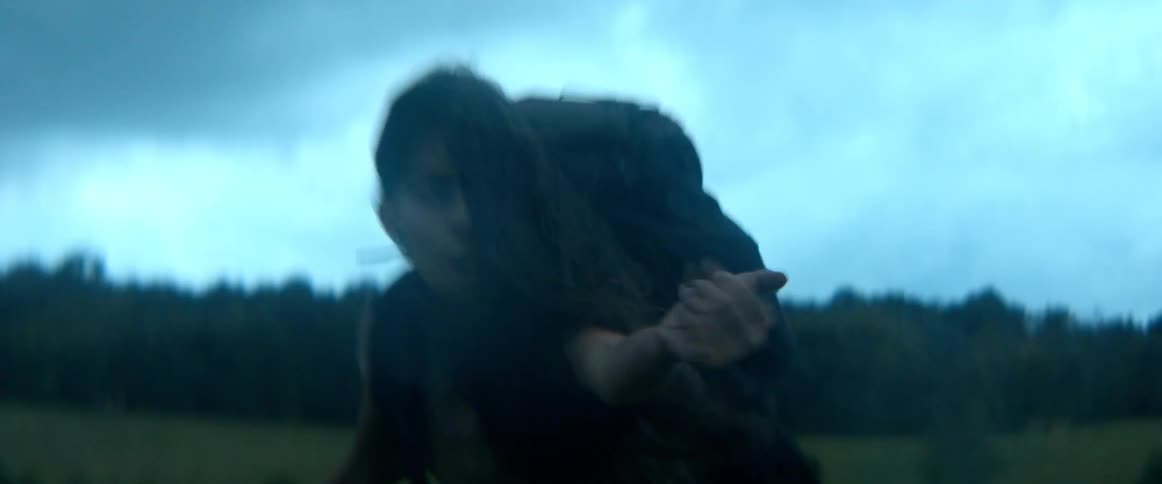 A terrified woman wearing a backpack runs for her life through a desolate field at dusk