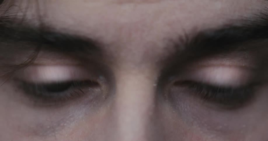 A man's tired eyes slowly open to reveal an intense stare in this dramatic close-up