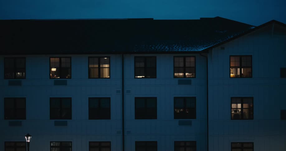 A quiet, snowy night falls over an apartment building with warm lights glowing from within