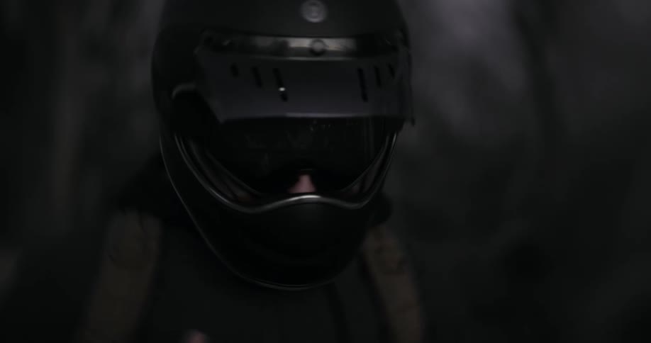 A motorcyclist's black helmet slowly comes into focus in a dark, moody setting, revealing a forest reflection in the visor
