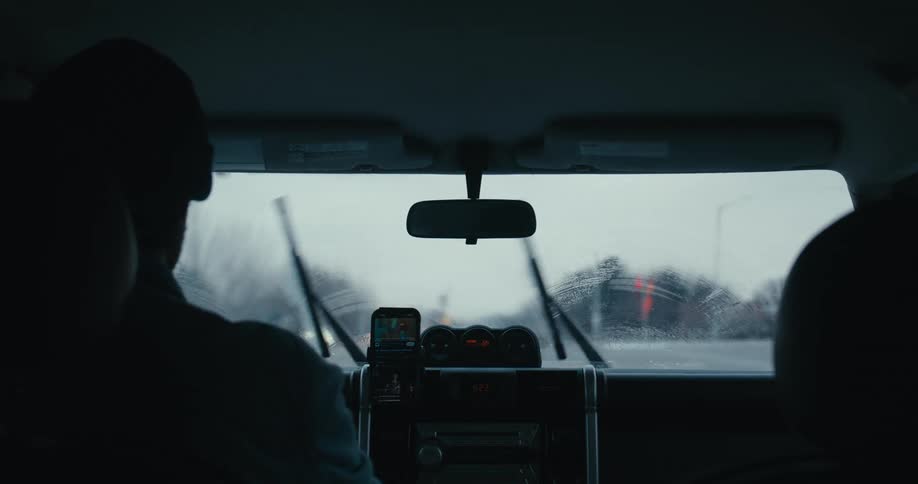 View from the backseat of a car as the windshield wipers clear away the rain on an overcast day