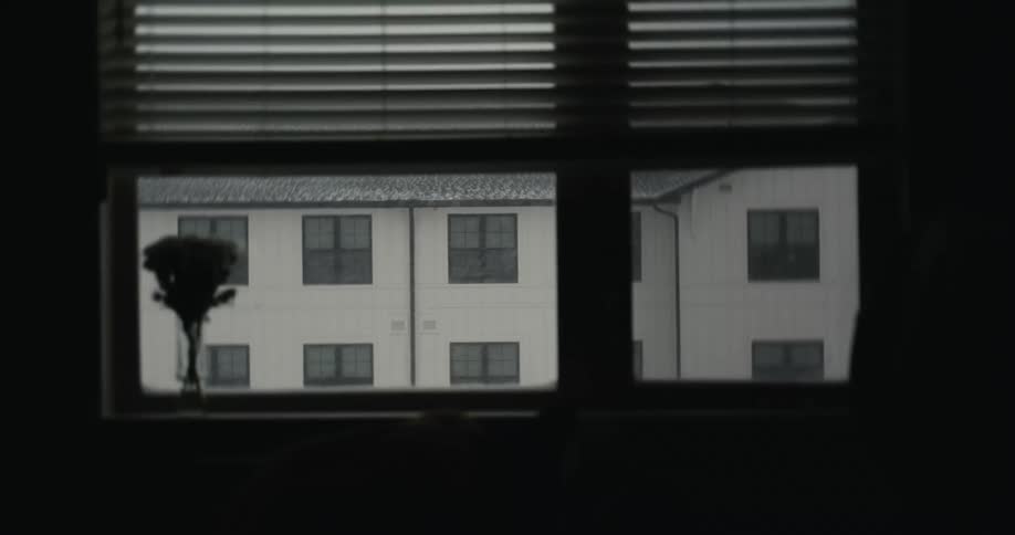 A gloomy view from a dark window as rain falls on a neighboring apartment building