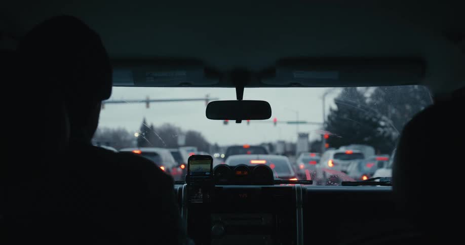 Over-the-shoulder shot of a driver checking their phone while stopped in traffic on an overcast day