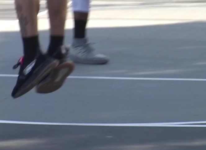 A shirtless man with tattoos jumps rope on an outdoor basketball court in slow motion