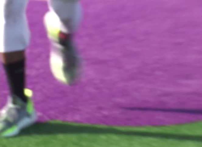 Close-up of a man's athletic shoes and quick feet as he trains on a colorful purple and green turf field