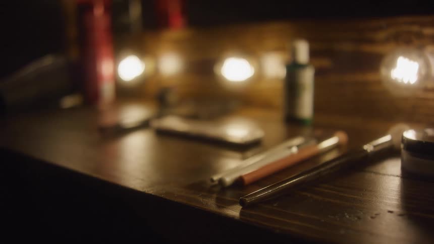 A slow rack focus reveals makeup brushes, cosmetics, and beauty products on a wooden vanity table in a warmly lit dressing room