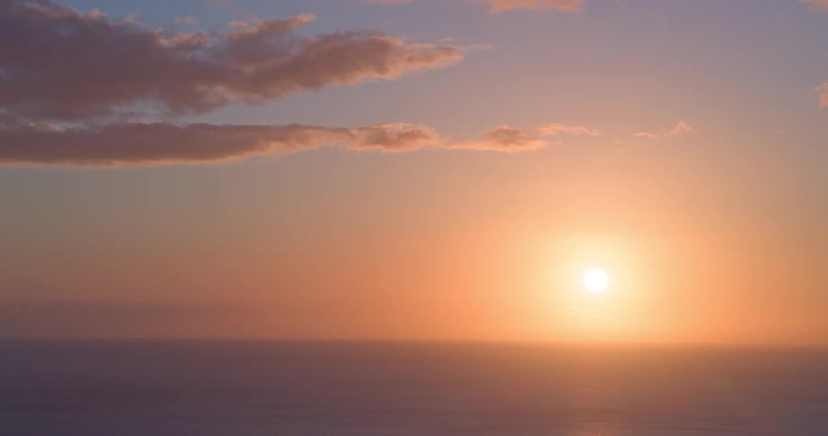 A serene and colorful sunset casts a golden glow over the calm ocean horizon