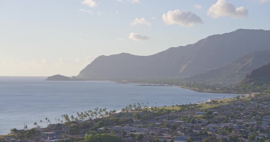 A scenic aerial view of a Hawaiian coastline reveals a small town nestled between the calm ocean and lush green mountains