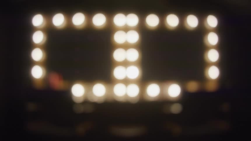 A static, out-of-focus shot of the glowing bokeh lights on a makeup vanity mirror in a dark room