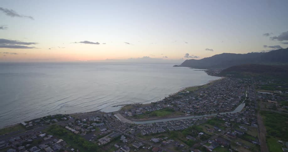 Wide high-angle shot of a tranquil Hawaiian coastal town nestled between the mountains and the sea at sunset