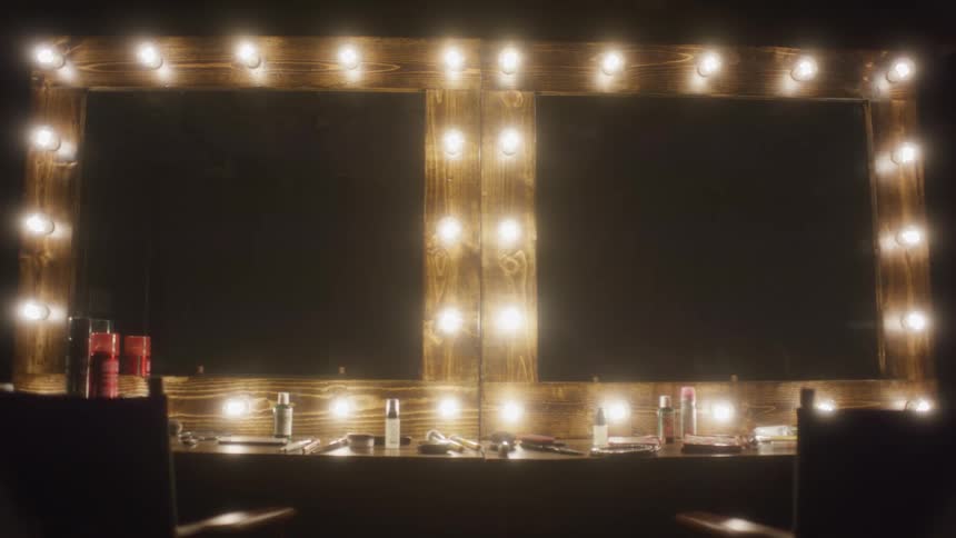 A backstage dressing room with two large vanity mirrors whose lights slowly dim to darkness
