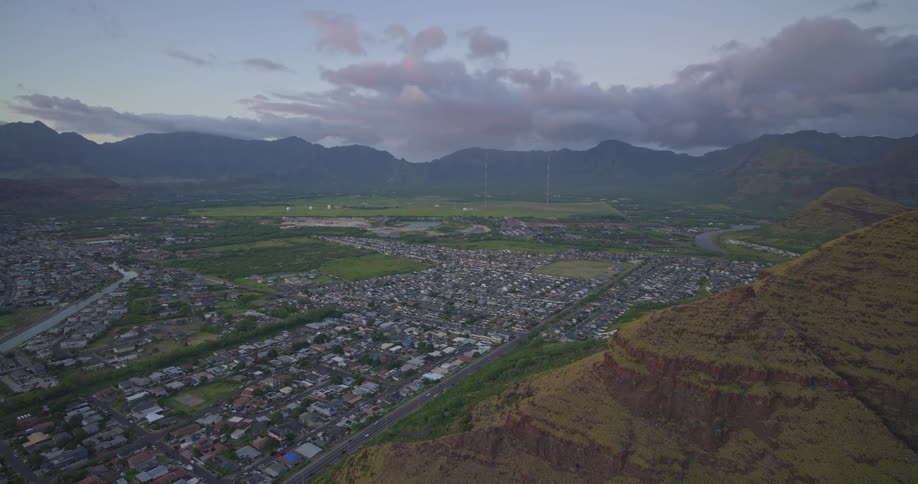 An expansive aerial shot slowly moves over a coastal town and lush valley in Hawaii at dusk