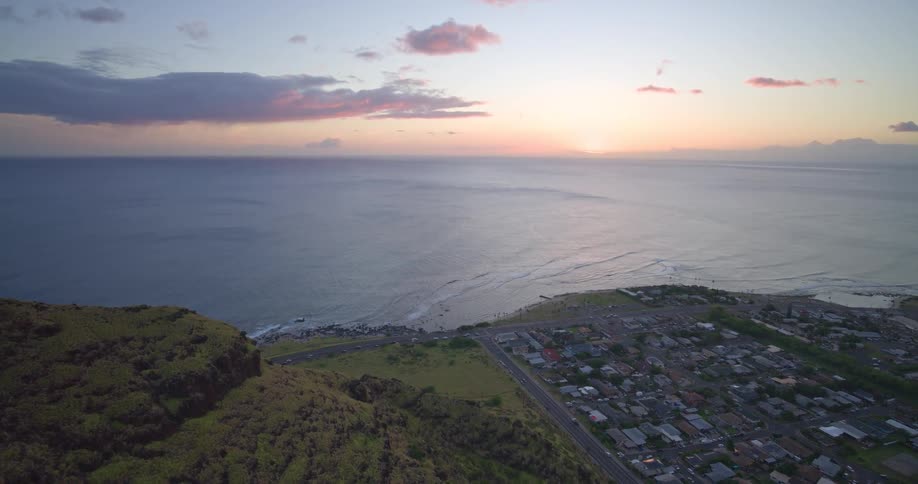 A majestic aerial view from a lush green cliffside reveals a coastal community and the vast Pacific Ocean at sunset