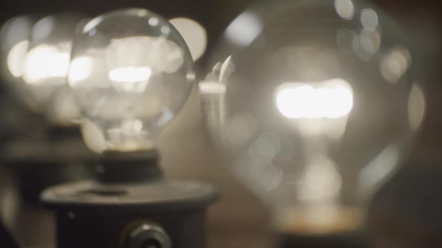 A row of vintage incandescent light bulbs glow with a warm light in this close-up slow-motion shot