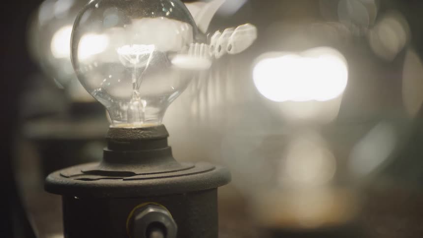 A close-up shot of a glowing vintage incandescent light bulb with a row of other bulbs creating a warm bokeh effect