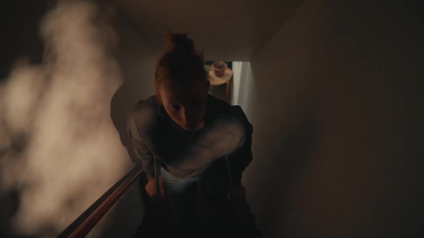Injured redhead woman with crutches makes her way up a dark staircase filled with smoke