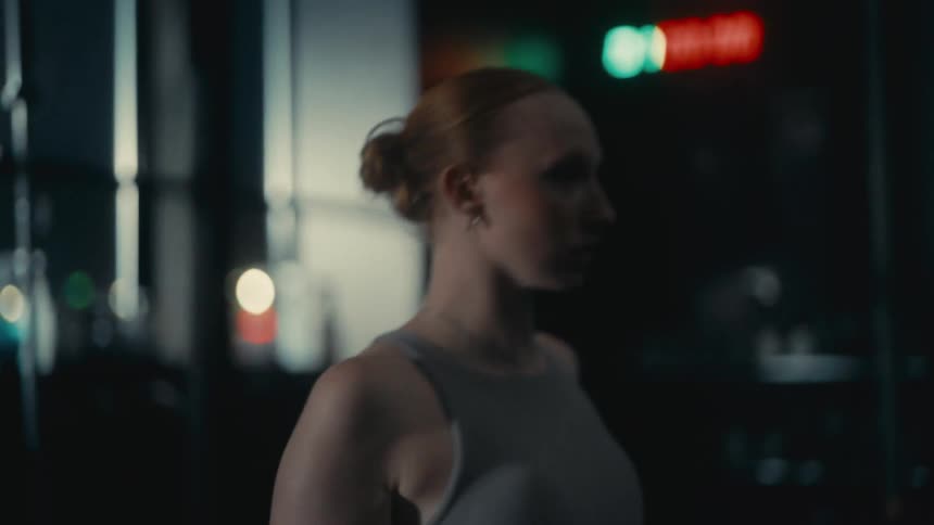 Profile view of a focused woman with red hair in a bun performing a cardio workout on a rower in slow motion