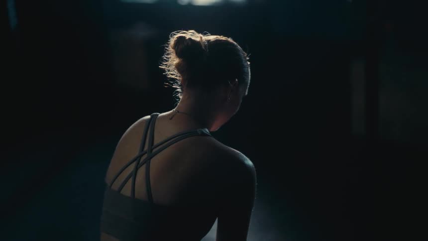 Cinemagraph of a woman with her hair in a bun, sitting with her back to the camera in a dark room illuminated by a single light