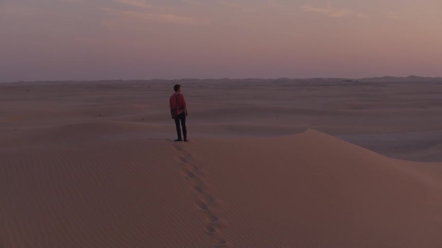 A man standing on a sand dune turns and walks across it