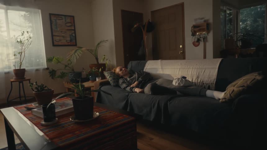 A woman relaxes and takes a nap on the couch in her dimly lit, cozy living room