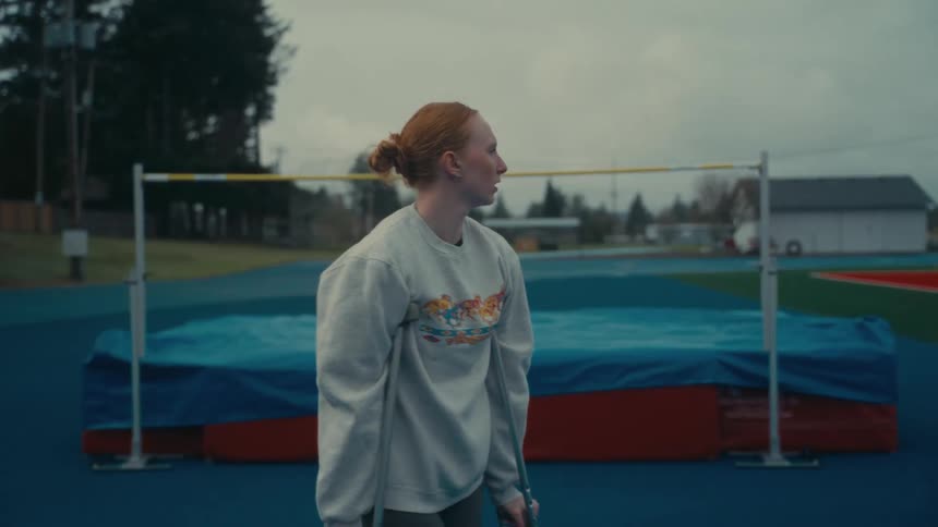 A frustrated female athlete on crutches looks at the high jump bar after suffering an injury