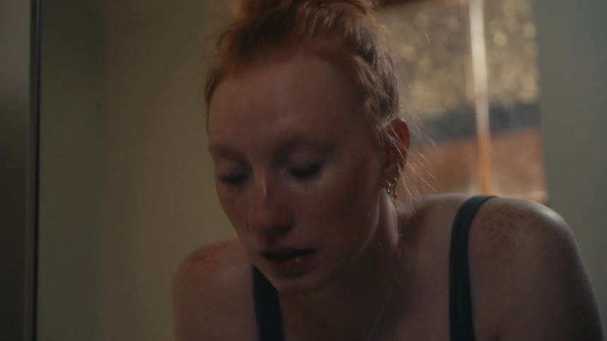 A sad young woman with red hair looks at her reflection as a tear rolls down her cheek