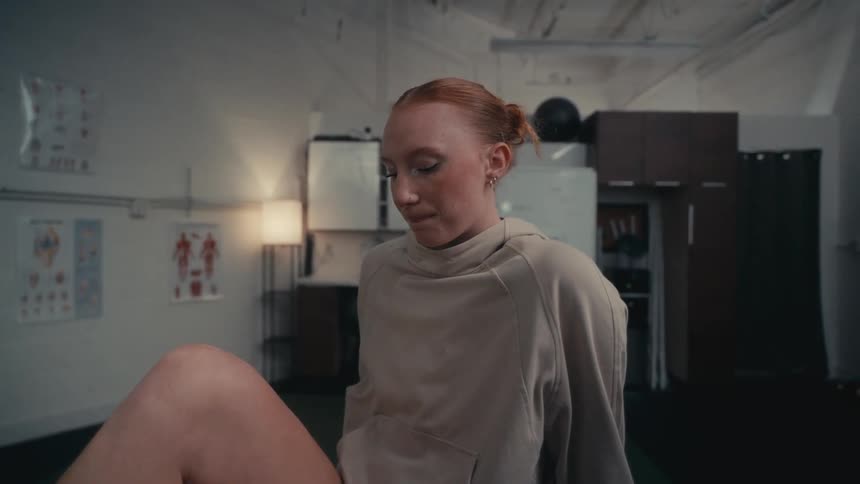 Close-up of a contemplative female athlete sitting in a dimly lit gym or clinic