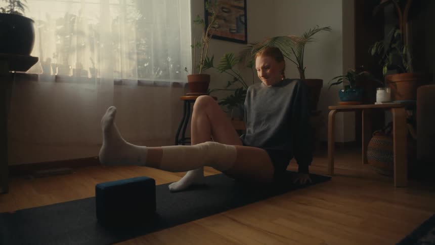 A determined woman carefully performs physical therapy exercises at home to rehabilitate her injured leg