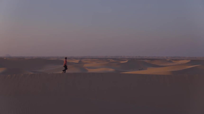 A man walks on a sand dune in a desert