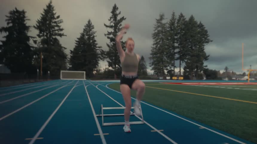 An athletic young woman in slow motion powerfully executes plyometric hurdle jumps on a blue track during a training session