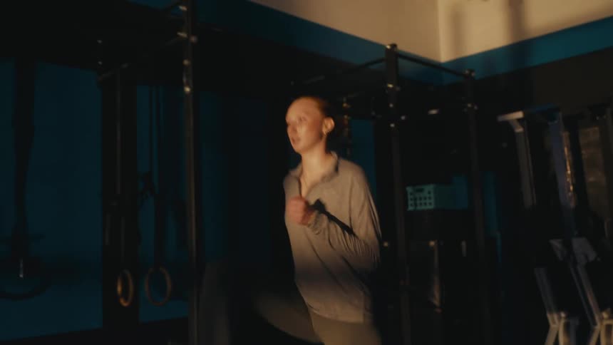 A fit young woman with red hair performs high knees as she warms up in a dark and atmospheric gym