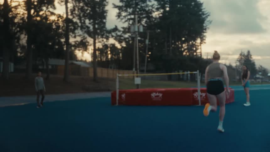 A female track and field athlete runs in slow motion towards the high jump bar during practice at dusk