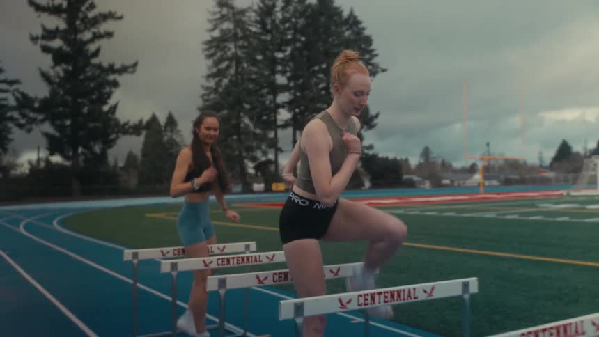 Two female athletes perform warm-up hurdle drills on an outdoor track during a training session