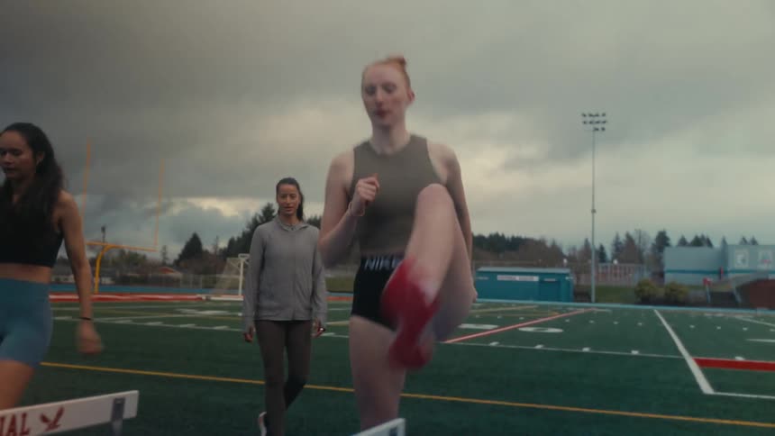 Young female athletes practice high-knee drills over hurdles on an outdoor track and field in slow motion