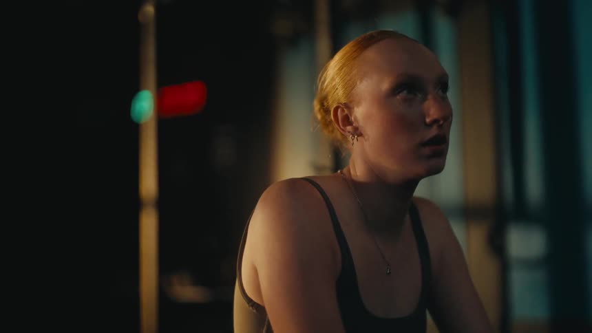 A determined female athlete catches her breath in slow motion during an intense workout in a dimly lit gym