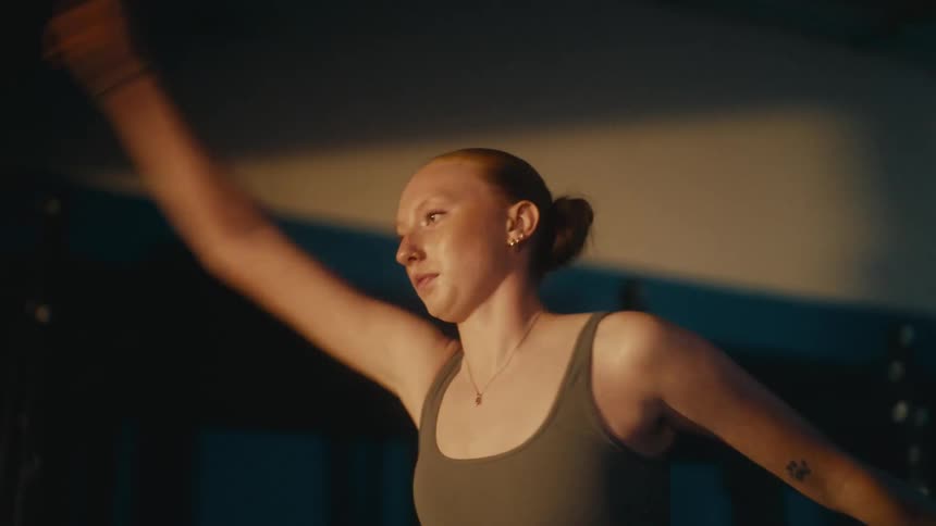 A focused young woman in athletic wear warms up by running in place and doing arm circles in a dimly lit gym