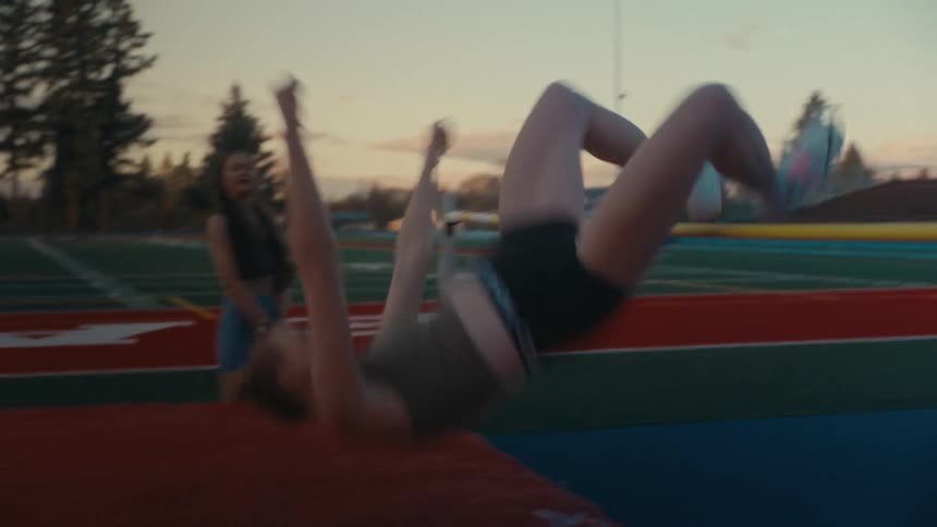 A female high jumper gracefully clears the bar in slow motion at a track and field stadium during a beautiful sunset