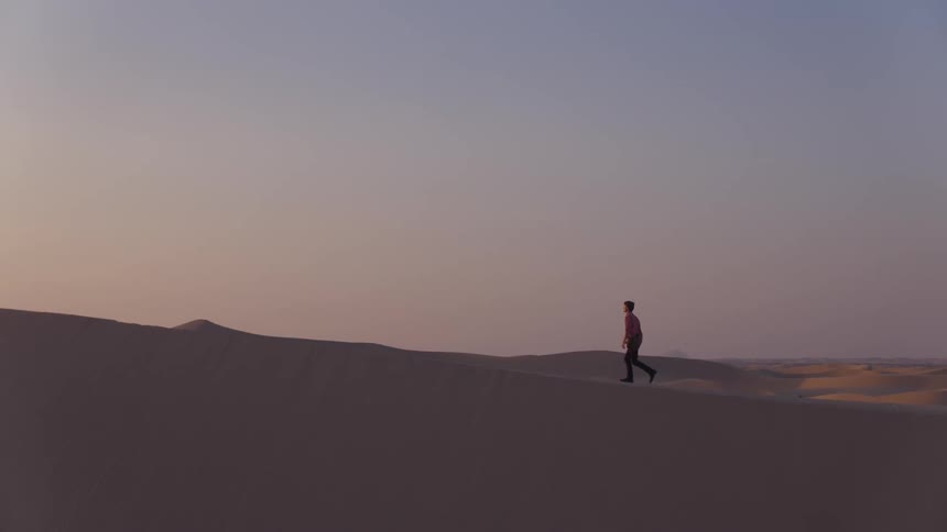A man walks on a sand dune in the desert