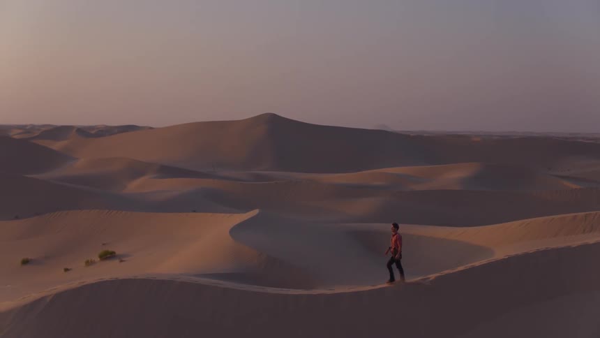 A man is walking across sand dunes at dusk