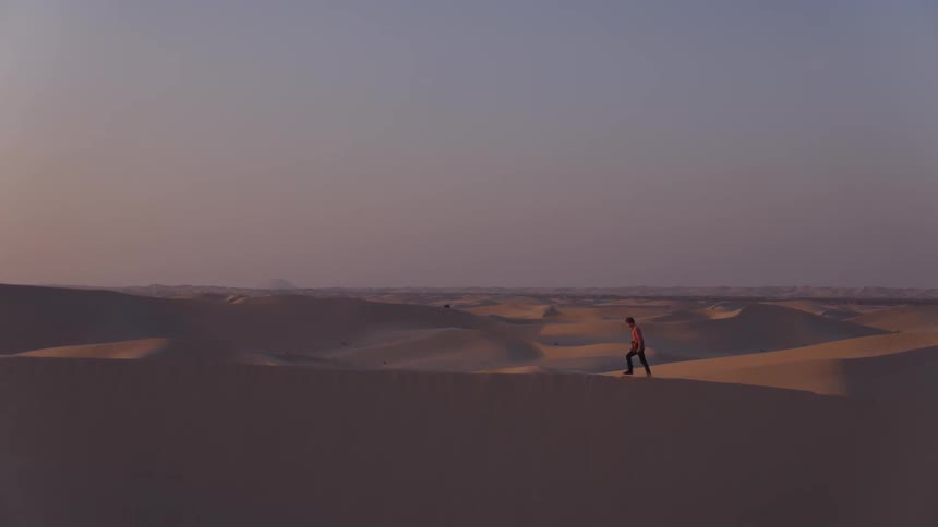 A man walks on a sand dune in a desert at sunset