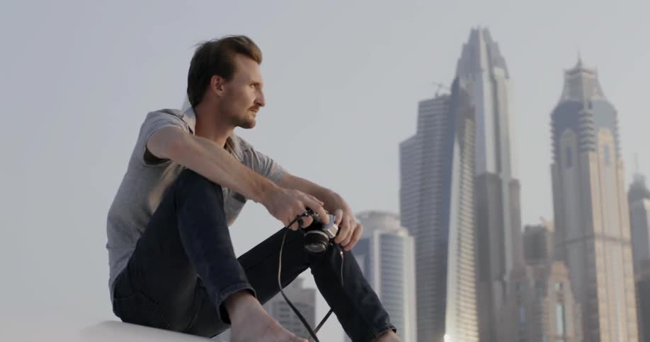 A man sits holding a camera in an urban setting