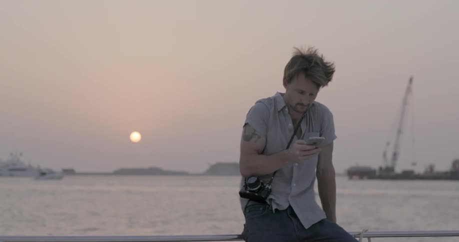 A man sitting on a boat at dusk is looking at his cellphone