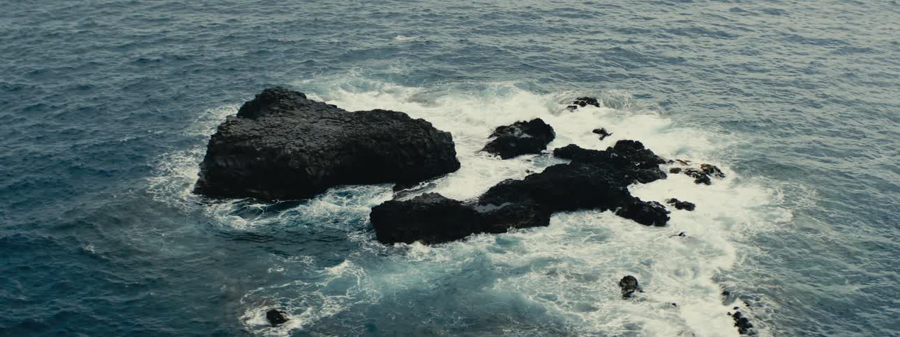 Dramatic high-angle shot of powerful ocean waves crashing against dark, rugged volcanic rocks