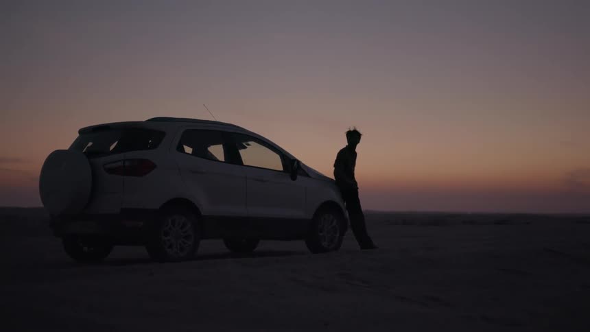 A man leans against his car at sunset
